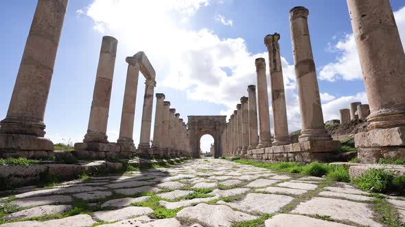 Corinthian Pillars And Stone Path Leading To Big Stone Arch In Roman Ruins In Jerash