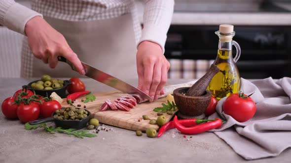 Woman Slicing Fuet Sausage with Knife at Domestic Kitchen