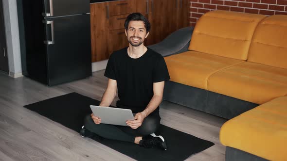 Portrait of a Man Sitting on the Mat on the Floor with Laptop at Home