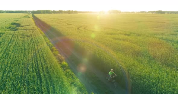 Aerial View on Young Boy That Rides a Bicycle Thru a Wheat Grass Field on the Old Rural Road