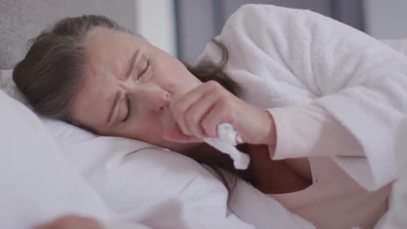 Sick woman with tissue coughing in bed at home