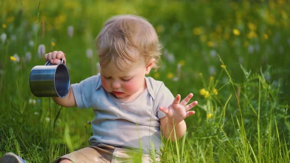 one year old baby spills liquid from a metal mug. The concept of walking outdoors,