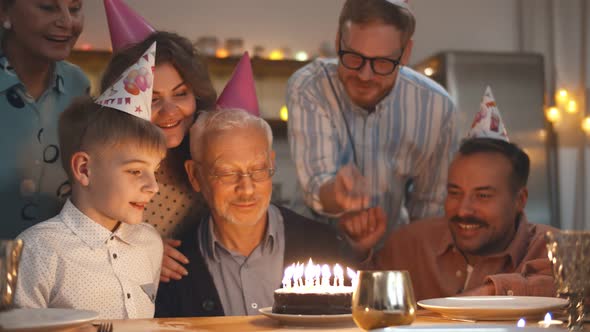 Gathering of Friends and Family at Birthday Party for Senior Man Blowing Out Birthday Candles