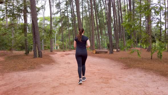 Girl running on a dirt trail between trees, cameraing from behing to the right side.