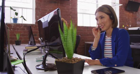 Diverse male and female business colleagues wearing headsets sitting at desks having video calls