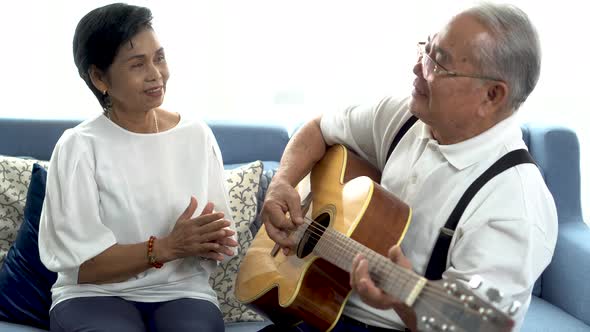 Happy Elderly Woman Clapping Hands While 70s Man Playing Guitar