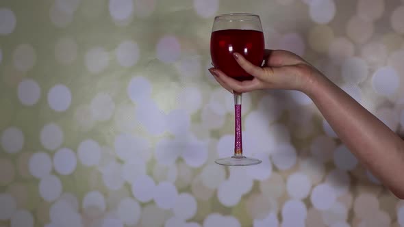 A woman's hand holding a glass of rose wine on a glittery background