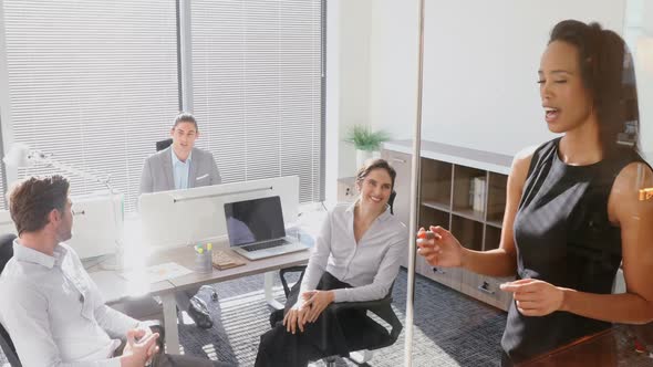 Female executive with his colleagues discussing over glass board 4k