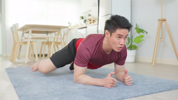 Asian handsome active young man doing plank on floor in living room.