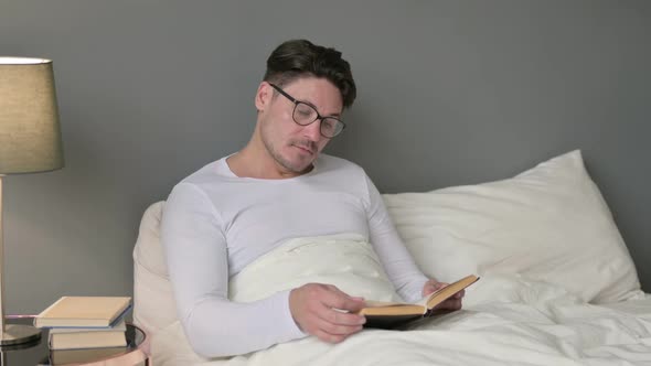 Middle Aged Man Reading Book in Bed