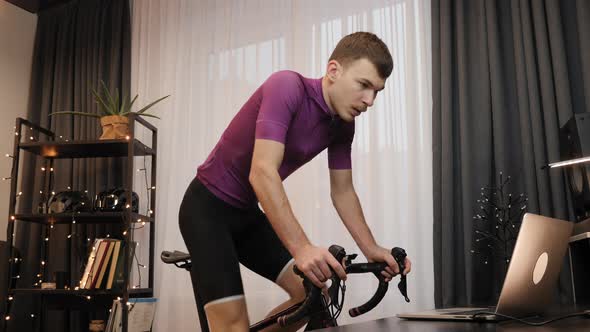 Man cyclist is cycling on indoor smart bike trainer. 