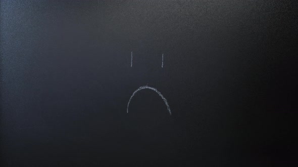 Man drawing sad smile emoticon icon on chalkboard