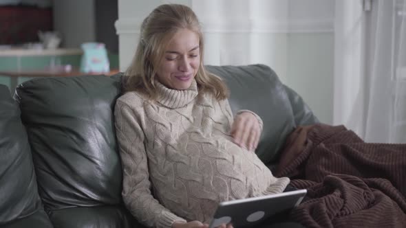 Attractive Pregnant Caucasian Woman Watching Video on Tablet and Talking To Her Belly