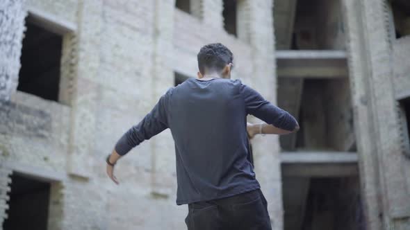 Back View of Agressive Young Man Drinking Beer and Shouting at Abandoned Slums. Mixed-race Alcoholic