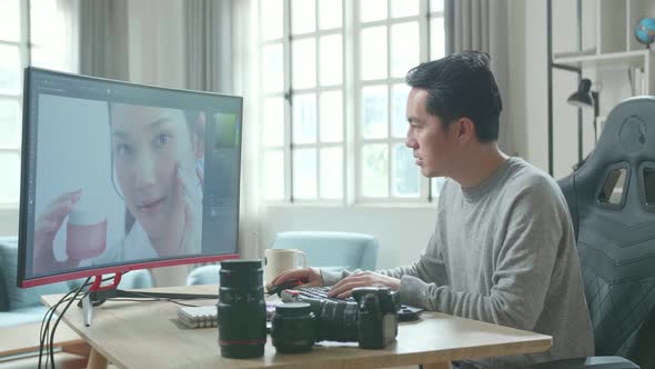 Asian Cameraman Using Desktop Computer For Editing Photos While Working At Home