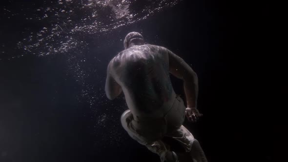 a Large Bald Man Without a Shirt Hovers in the Dark Under the Water in the Pose of a Baby