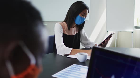 Asian woman wearing face mask using digital tablet while sitting on her desk at modern office