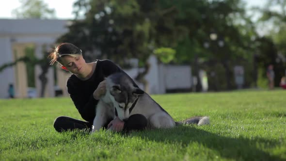 Beautiful Young Woman Playing with Funny Husky Dog Outdoors in Park at Sunset or Sunrise on Green