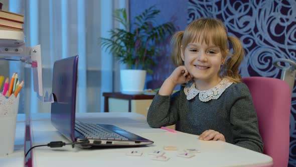 Child Girl Doing School Homework Writes in Notebook Using Laptop Computer at Home Online Education