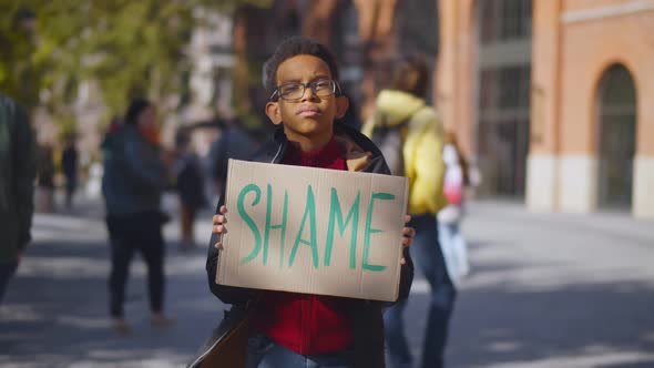 Portrait African Schoolboy Standing Near School Building and Holding Cardboard Sign with Shame Text