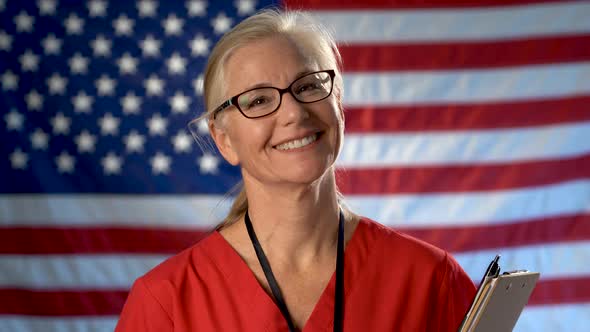 Portrait of a nurse nodding her head and smiling against an out of focus US flag.