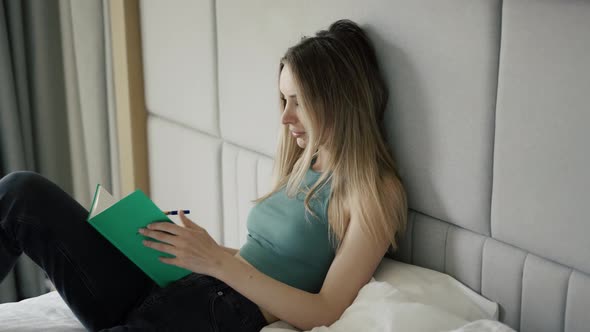 Young Woman is Sitting on Bed at Home and Writing in Diary