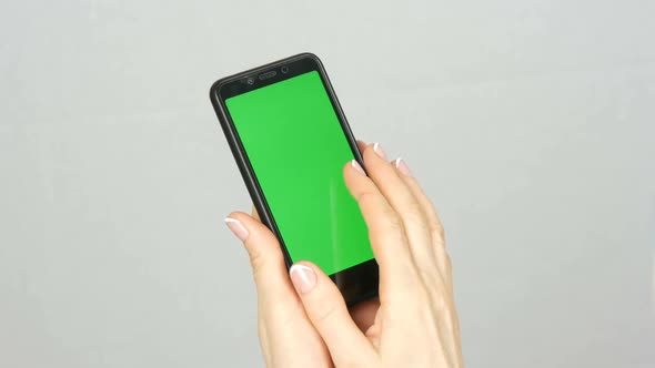 Wellgroomed Neat Female Hands with a Beautiful Manicure Hold a Black Smartphone with a Green Screen