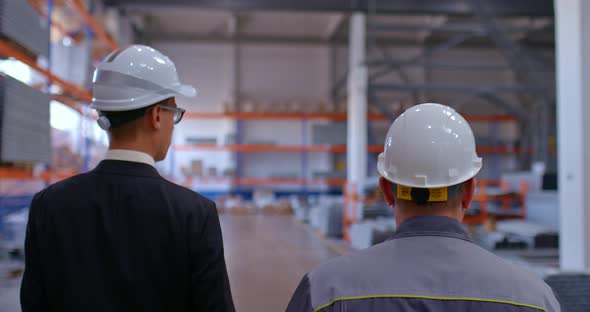 Director of the Plant and the Employee are in Protective Helmets in the Warehouse of the Plant