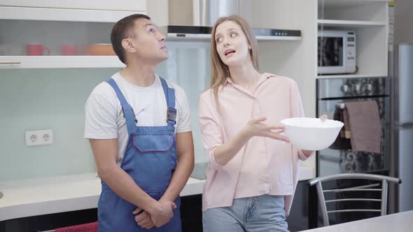 Sad Caucasian Woman and Service Man Looking at Water Drops Falling From Ceiling and Talking