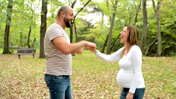 Handsome Man and Young Happy Pregnant Woman Rejoice Together in Park