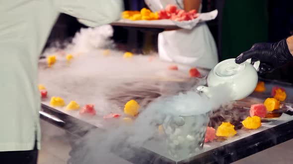 Chef and his assistant are putting fruit on the ice-cream background with steam. 