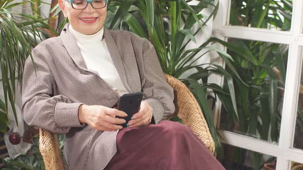 Beautiful Businesswoman Sitting in Business Center with Plants Aroud Talking on Phone