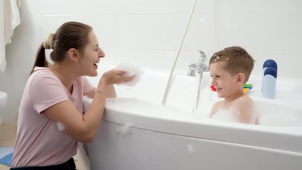 Happy Laughing and Smiling Mother with Son Playing in Bath with Soap Foam