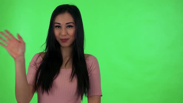 Young Attractive Asian Woman Waves with Hand - Green Screen Studio