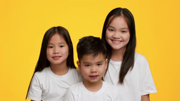 Two Happy Japanese Sisters And Little Brother Posing Yellow Background