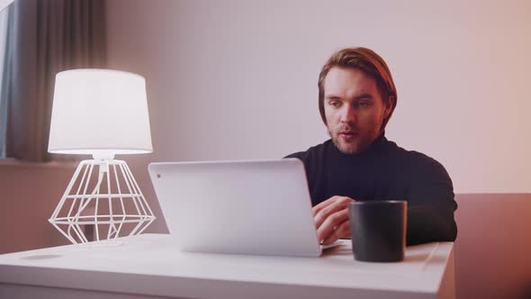 Caucasian Man Using Laptop at Home with Cup of Coffee Nearby