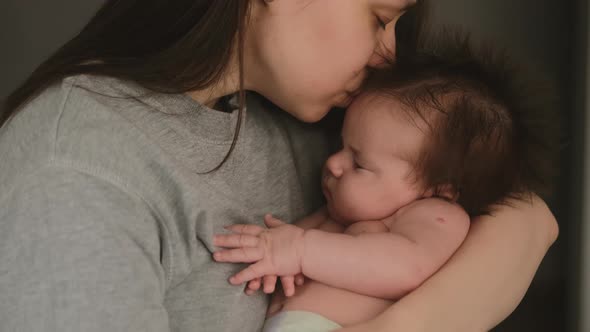 Authentic young mother holding newborn baby in her arms  kissing in head, lulls to sleep