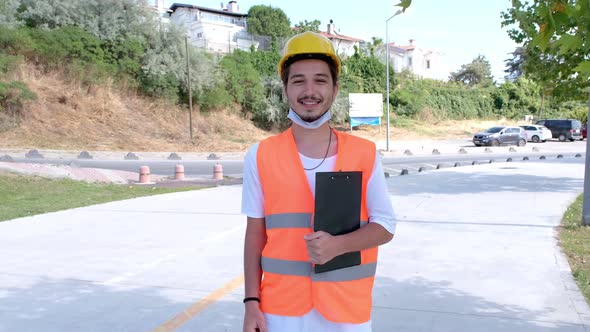 Portrait of young construction worker with white hardhat and face mask at construction site.