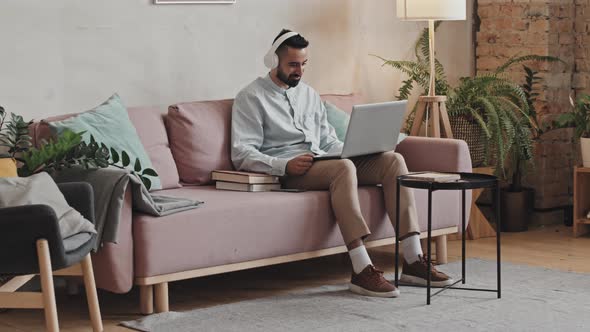 Man in Headphones Using Laptop in Living Room at Home