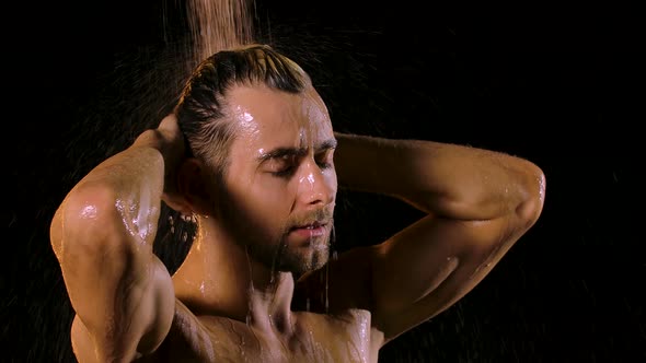 Attractive Muscular Young Man Enjoying a Shower with Closed Eyes on a Black Background