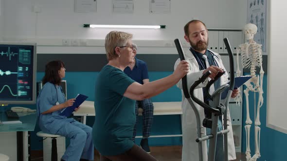 Male Doctor Helping Elder Woman to Use Stationary Bicycle