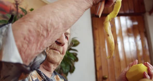 Portrait of an Old Wrinkled Woman Who Enthusiastically Peels Potatoes Creating a Long Spiral of