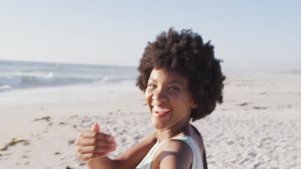 Portrait of smiling african american woman holding hand on sunny beach