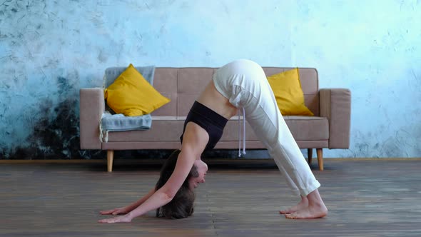 Cute Brunette Woman Does Yoga Exercises at Modern Home at Sofa Background