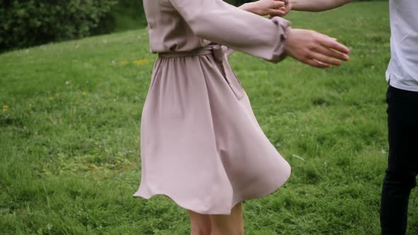 Man with a Woman Blonde in a Dress Dance on a Green Field in Nature in Summer