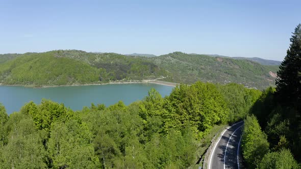 AERIAL - Maneciu dam, forest and mountain road in Romania, lowering wide shot