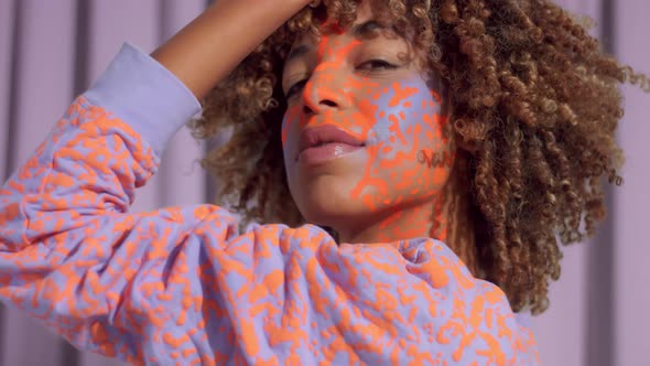 Mixed Race Woman with Curly Hair and Bright Neon Makeup Pattern on the Face the Same Like on Her