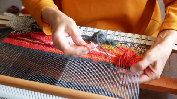 Weaver is tying knots to create a cut pile carpet effect. Making coloured and textured tapestry