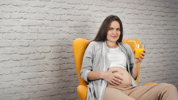 Charming Young Pregnant Girl Touching Naked Belly Holding Glass with Refreshing Vitamin Orange Juice