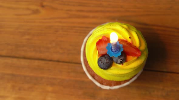 Top View of a Festive Cupcake with Yellow Cream with a Burning Candle Rotating on a Light Pink
